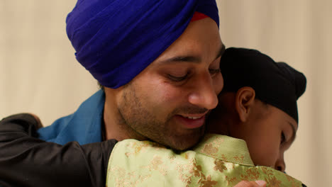 Close-Up-Studio-Shot-Of-Sikh-Father-Embracing-Son-Both-Wearing-Turbans-Against-Plain-Background-5